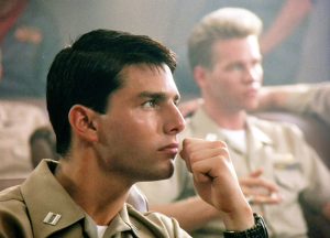 Tom Cruise as Maverick in profile, fist to chin, focused in Top Gun briefing room, 1986 film still.
